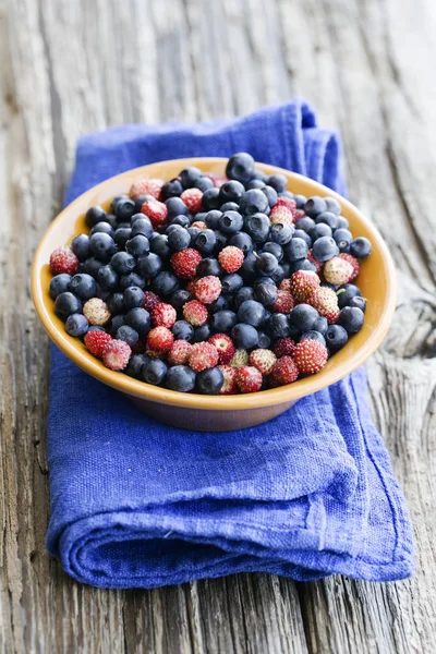 fresh wild strawberries and blueberries in bowl on blue linen cloth on wooden table