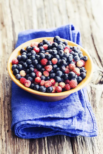 fresh wild strawberries and blueberries in bowl on linen cloth on wooden surface