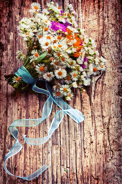 bouquet of bright filed flowers with ribbon on vintage wooden surface