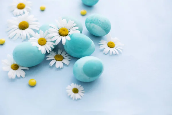 Renkli Paskalya yumurtaları ve papatya çiçekler üzerinde mavi arka plan ile natürmort