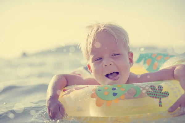 Toddler boy floating in swim ring, summer vacation background