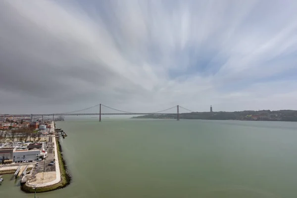 Široké triko pohled 25 de Abril Bridge v Lisabonu přes řeku Tejo, ultra dlouhé expozice — Stock fotografie