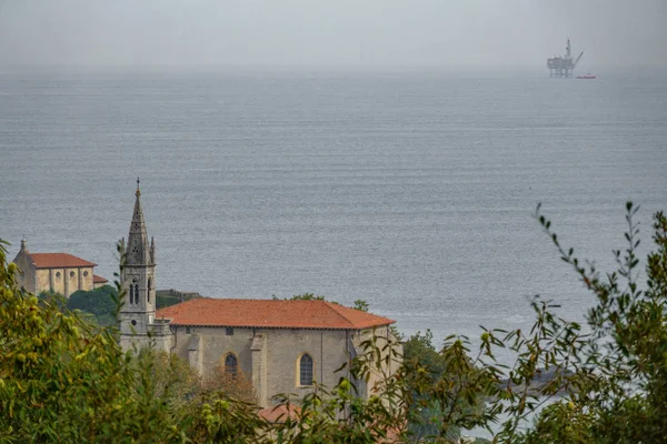 Iglesia de Mundaka con plataforma oceánica de gas en el horizonte — Foto de Stock