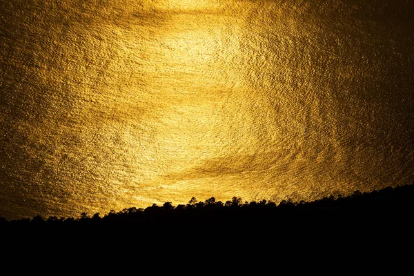 Riflessione tramonto dorato nell'oceano vicino alla costa scura — Foto Stock