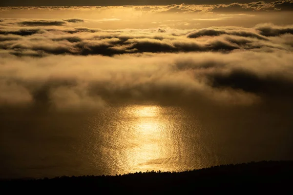 Reflejo dorado del atardecer en el océano cerca de la costa oscura sobre las nubes —  Fotos de Stock