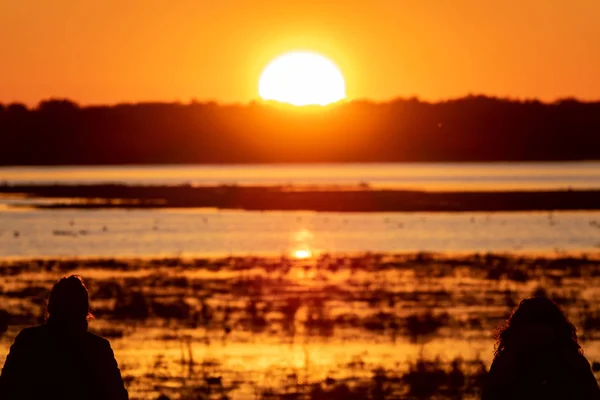Две женщины силуэты наблюдают восход солнца над озером — стоковое фото