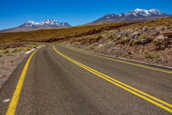 Atacama zakřivená silnice a sníh pokryté sopkami — Stock fotografie
