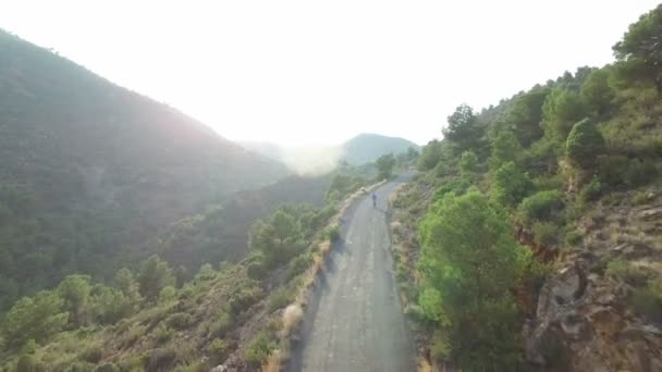 Luchtfoto van fietser op hoge helling bergweg tegen zon — Stockvideo
