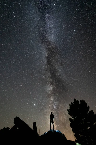 天の川が見える岩の上の夜の1人シルエットの背面図 — ストック写真