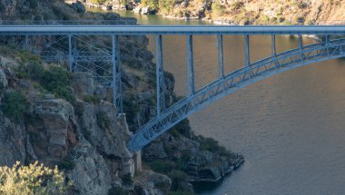 Zarif çelik bir köprü, sakin bir nehrin üzerindeki kayalık bir kanyonu kaplar ve etkileyici mühendisliği doğal güzellikle harmanlar..