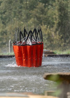 Asılı bir itfaiye kovası nehir suyunu topluyor, bu da güçlü sıçramalara neden oluyor..