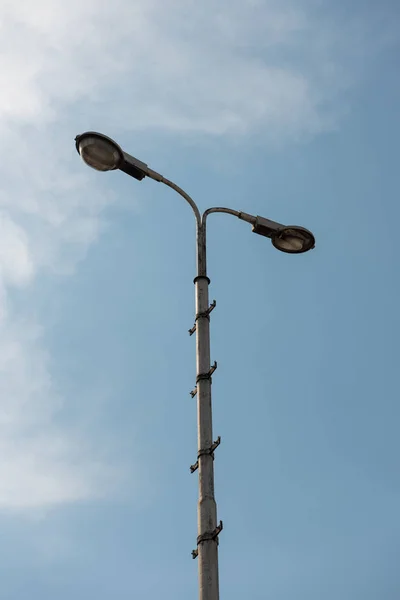 Old industrial street lamp against blue sky with white clouds.