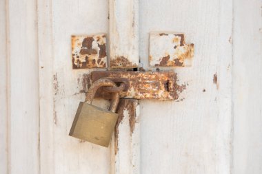 Eski ve paslı metal asma kilit beyaz kapı. Kapalı kapının kilidi ile.
