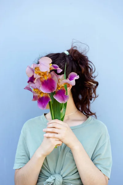 Un brillante ramo de flores iris sobre un fondo azul sostiene a una chica en sus manos, cubre su cara — Foto de Stock