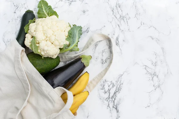 Set of products in a cotton eco bag on a marble table, bananas, avocado, eggplant, zucchini, cauliflower. The concept of zero waste. copy space.