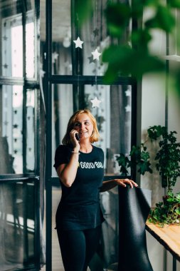 Bir güzel kızıl saçlı genç gülümseyen kız siyah t-shirt ve tozluk telefonunu, yoga Studio kullanır ve bir mat tutun