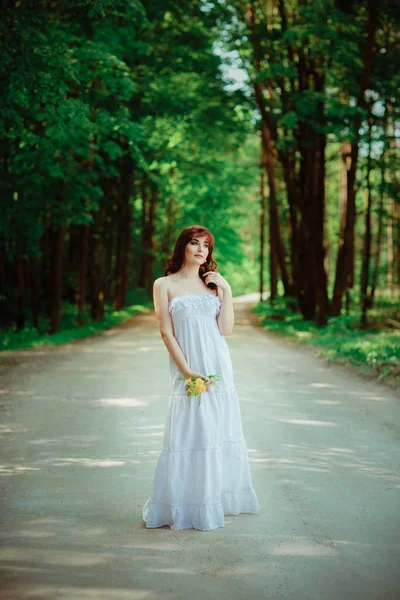 Hermosa chica con flores de diente de león en carretera forestal — Foto de Stock