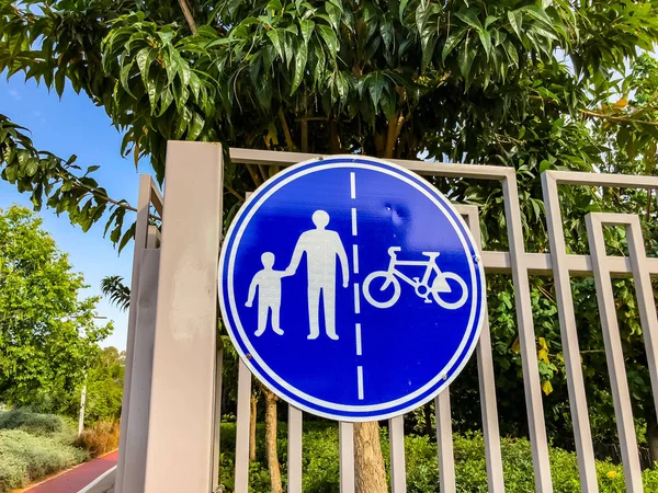 Sign for pedestrians and cyclists on a white fence near a road in the park — Stock Photo, Image