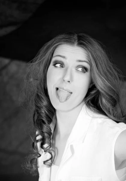 어두운 배경에서 흰색 셔츠 스탠드 스튜디오 촬영에 혀를 보여주는 아름 다운 여자. — 스톡 사진