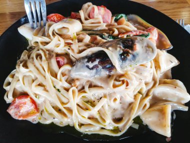 Midye makarna ile masanın üzerinde siyah bir tabak içinde pişirilir.