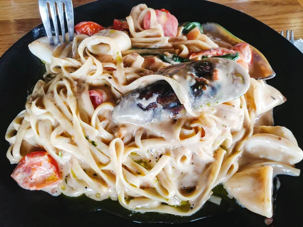 Midye makarna ile masanın üzerinde siyah bir tabak içinde pişirilir.