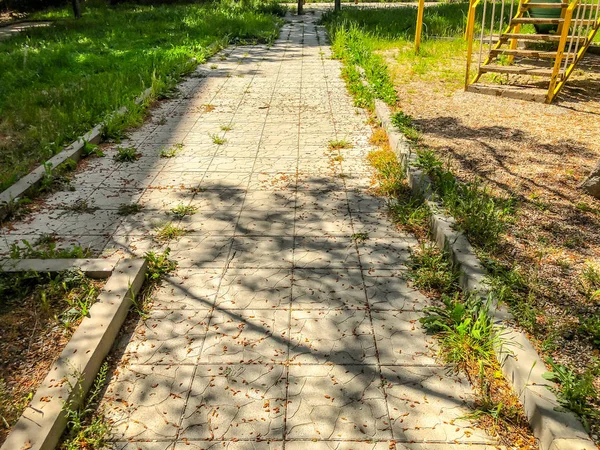 A estrada é um caminho de pedra vai para o pátio de um edifício residencial, um quintal com grama verde . — Fotografia de Stock