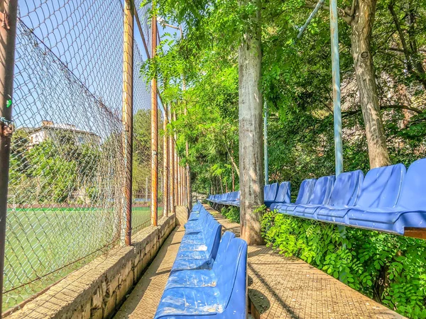 Bancos de plástico e árvores floridas no parque da cidade perto do estádio — Fotografia de Stock