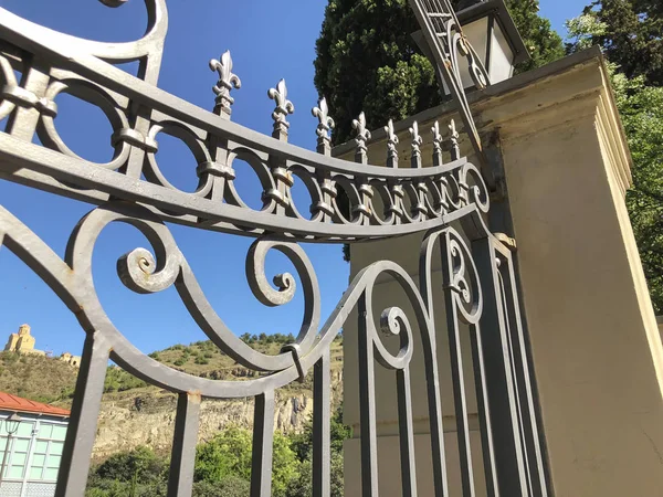 Entrada al jardín botánico de Tiflis. Hermosa puerta de hierro contra el cielo azul. Día de verano en la ciudad — Foto de Stock