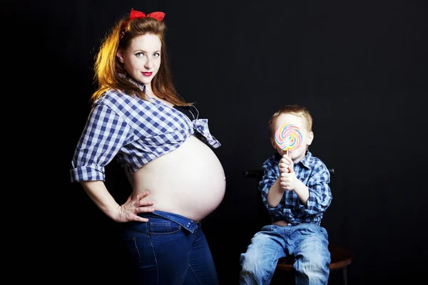 Modieuze roodharige vrouw in pin-up stijl met haar zoon met een lolly in studio — Stockfoto