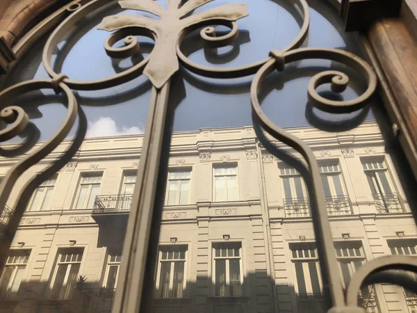 Weerspiegeling van een gebouw op de straat in een houten deur van glas met een ijzeren decoratieve ornament. Oude Tbilisi architectuur — Stockfoto