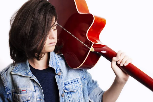 Side view portrait of a teenager wearing denim jacket in studio background while holding a guitar. — Stock Photo, Image