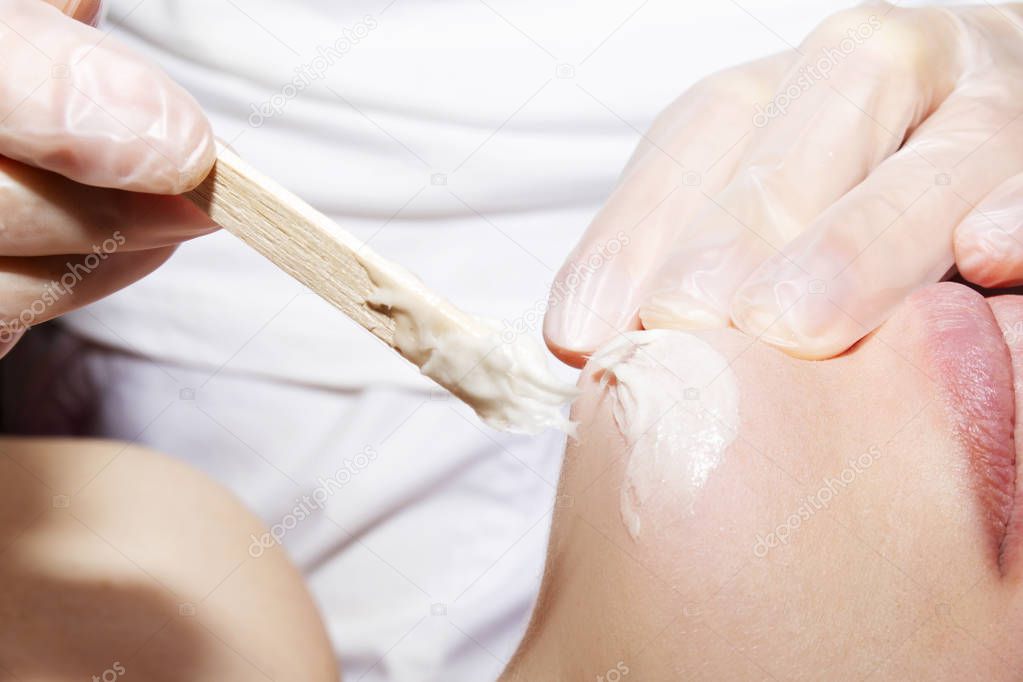 Depilation with hot wax mustache in the beauty salon. Young woman receiving facial epilation close up. Cosmetologist removes hair on face. Beauty salon, mustache depilation.