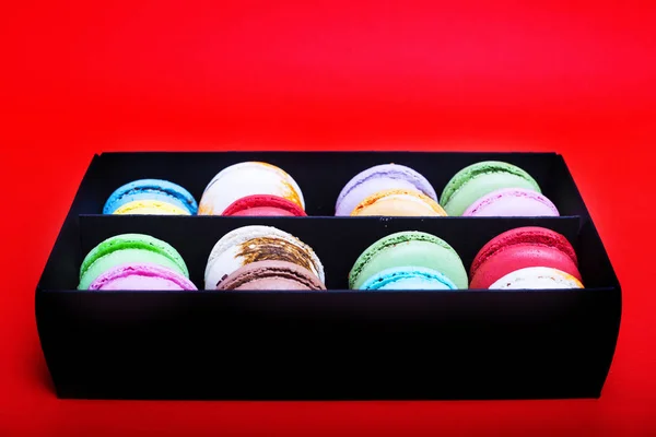 Tasty different colored macarons in black box on red background — Stock Photo, Image