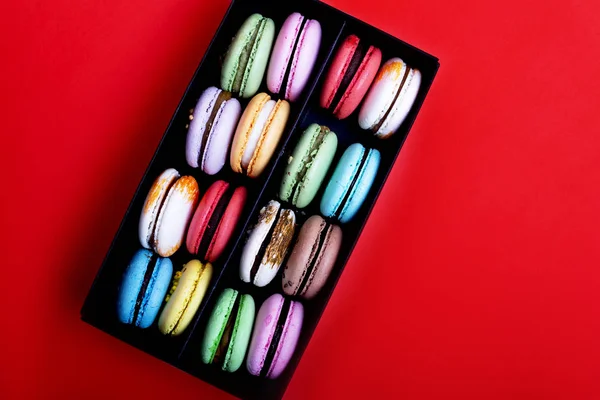 Tasty different colored macarons in black box on red background — Stock Photo, Image