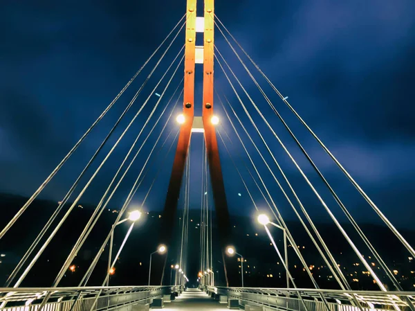 Trottoaren område som går igenom en kabel-stannade bro med stora stålkablar, närbild nattetid i starkt ljus — Stockfoto