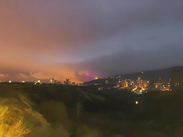 Night view opening on to the valley. Trees against the night sky. City lights in the distance — Stock Photo, Image