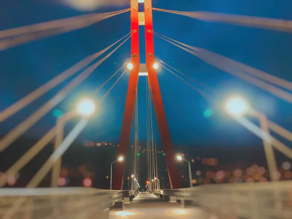 Área de calçada passando por uma ponte de cabo-permanecido com cabos de aço grandes, close-up à noite em luzes brilhantes. Efeito Borrão — Fotografia de Stock