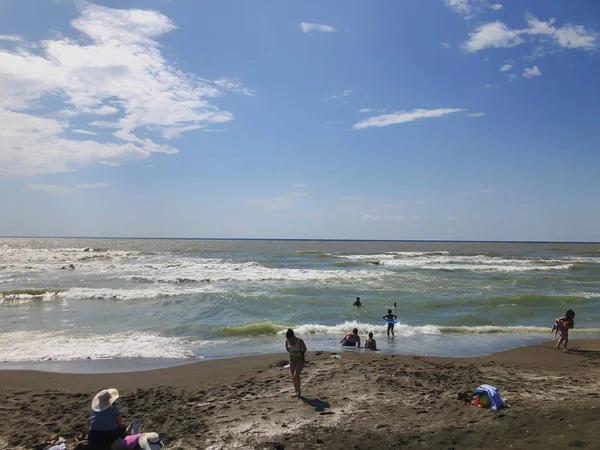 Utsikt över havet under solnedgången. Folk simmar i havet. Glitter vågor på en sandstrand. Sommar solig dag, vatten bakgrund — Stockfoto