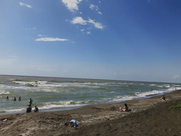 Utsikt över havet under solnedgången. Folk simmar i havet. Glitter vågor på en sandstrand. Sommar solig dag, vatten bakgrund — Stockfoto