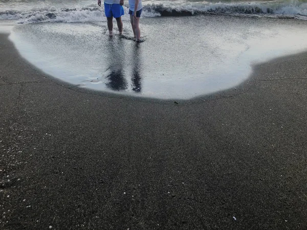 Reflexiones de personas de pie en la orilla del mar. Olas brillantes en una playa de arena. Día soleado de verano, fondo arenoso —  Fotos de Stock