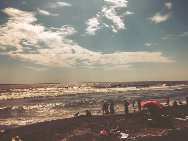 Uitzicht op de zee tijdens zonsondergang. Mensen zwemmen in de zee. Glitter golven op een zandstrand. Zomer zonnige dag, water achtergrond — Stockfoto