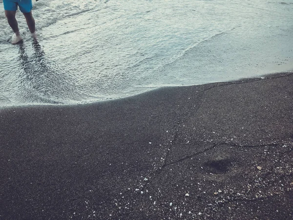 Ноги людини, що стоять на березі моря. Блискучі хвилі на піщаному пляжі. Літній сонячний день, піщаний фон — стокове фото