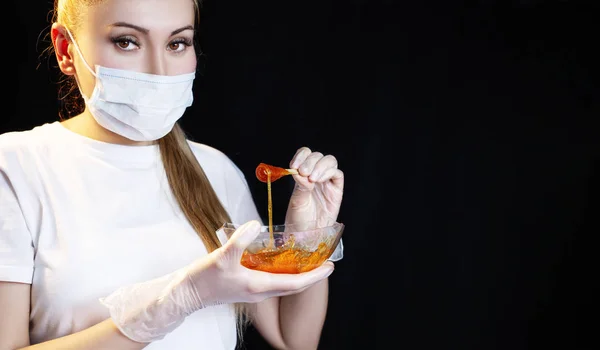 Woman with sugar hair removing paste on black background.