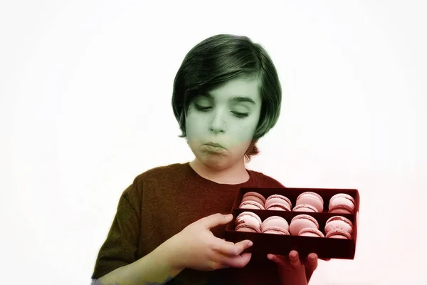 Knappe jongen houdt in zijn handen macaroni over witte achtergrond. — Stockfoto