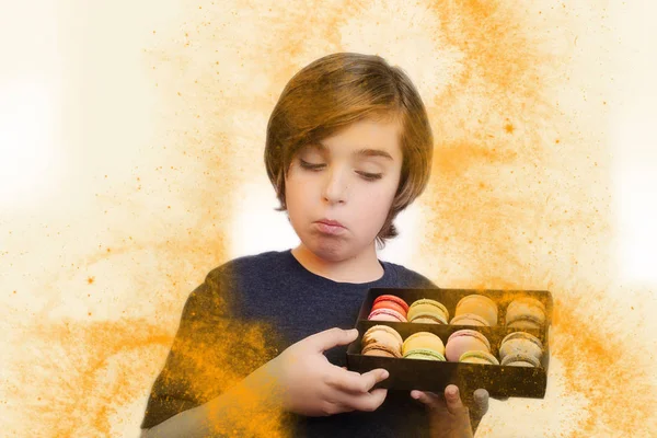 Knappe jongen houdt in zijn handen macaroni over witte achtergrond. — Stockfoto
