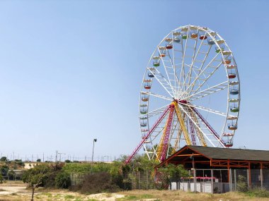 büyük beyaz dönme dolap ile arka planda bir gökdelen mavi gökyüzü karşı vurgulanır