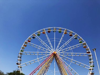 büyük beyaz dönme dolap ile arka planda bir gökdelen mavi gökyüzü karşı vurgulanır