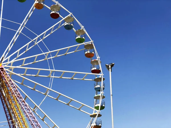 A large white Ferris Wheel with a skyscraper in the background is highlighted against a blue sky — Stock Photo, Image