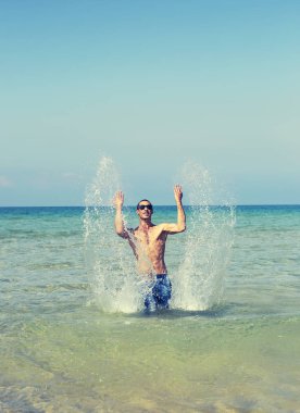 Genç maço erkek, kaslı seksi vücudu olan, denizdeki dalgalarla oynayan bir sporcu.