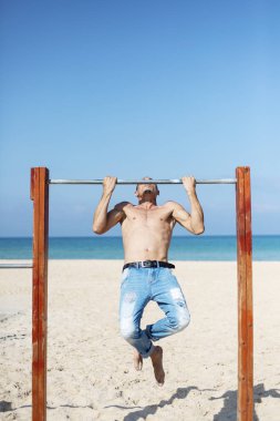 Çıplak gövdeli bir erkek sporcu yatay bir barda antrenman yapıyor. 